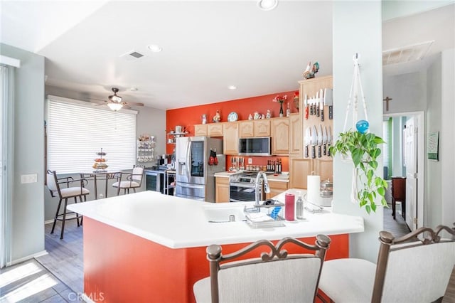 kitchen featuring ceiling fan, hardwood / wood-style floors, kitchen peninsula, appliances with stainless steel finishes, and light brown cabinets