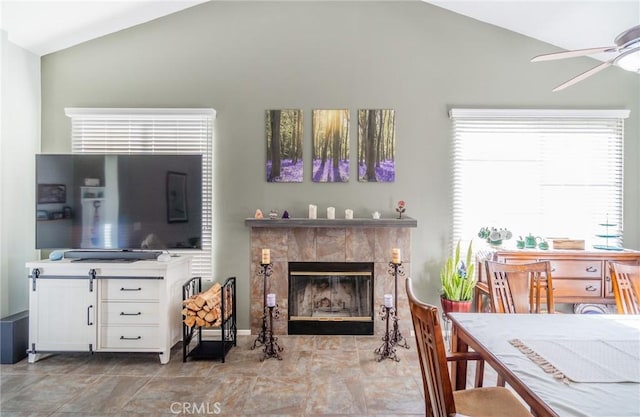 living room with a tiled fireplace, vaulted ceiling, and ceiling fan