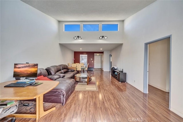 living room with a high ceiling, a textured ceiling, baseboards, and wood finished floors