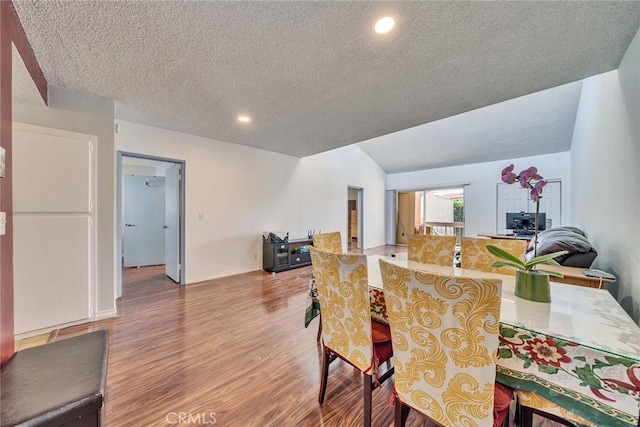 dining room featuring vaulted ceiling, hardwood / wood-style floors, and a textured ceiling