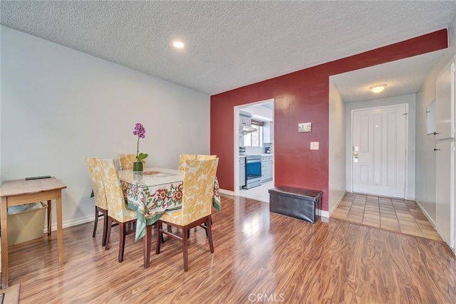 dining space with a textured ceiling, baseboards, and light wood-style floors