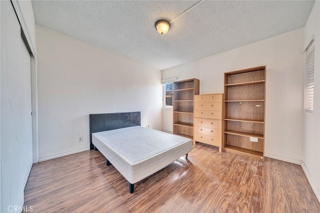 bedroom featuring a closet, a textured ceiling, baseboards, and wood finished floors