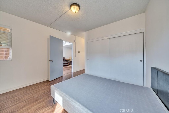 bedroom with a textured ceiling, a closet, wood finished floors, and baseboards