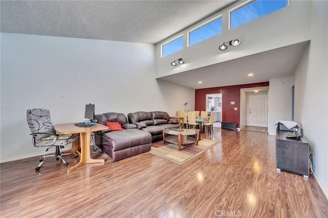 living room with baseboards, a textured ceiling, a high ceiling, and wood finished floors