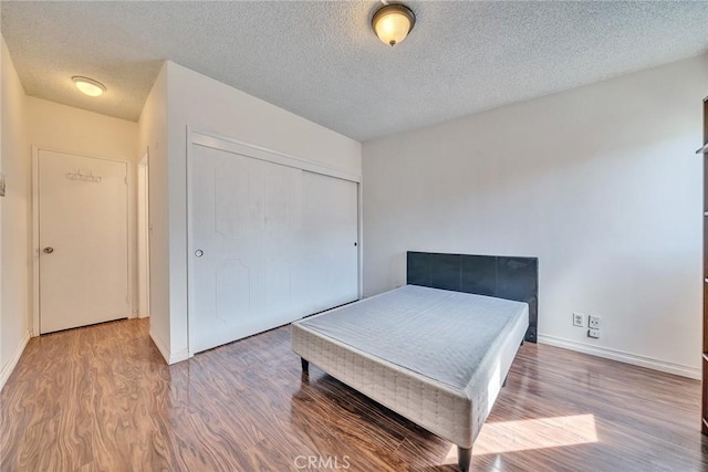 bedroom featuring a textured ceiling, a closet, baseboards, and wood finished floors