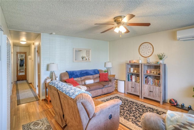 living room featuring a wall unit AC, ceiling fan, a textured ceiling, and light hardwood / wood-style flooring