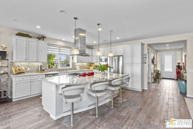 kitchen featuring a kitchen bar, island exhaust hood, appliances with stainless steel finishes, decorative light fixtures, and a center island