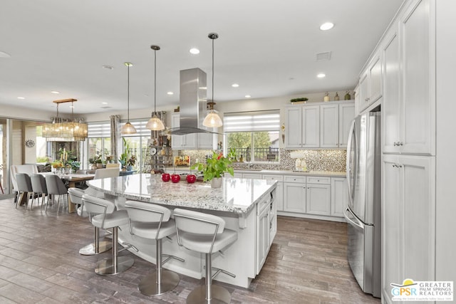 kitchen with white cabinets, a kitchen island, tasteful backsplash, island range hood, and stainless steel refrigerator