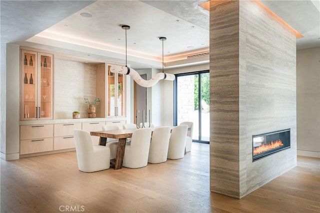 unfurnished dining area with light hardwood / wood-style flooring, a raised ceiling, and a fireplace