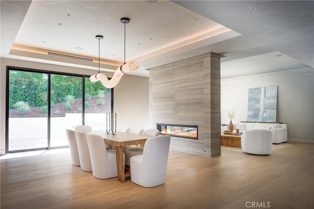 unfurnished dining area with light hardwood / wood-style flooring, a fireplace, and a raised ceiling