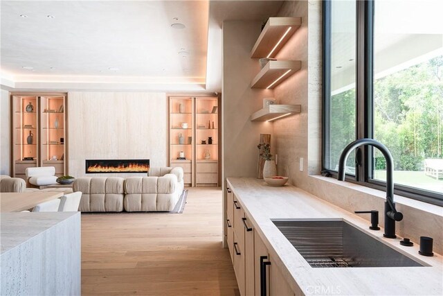 kitchen with sink, a large fireplace, light brown cabinets, and light hardwood / wood-style flooring