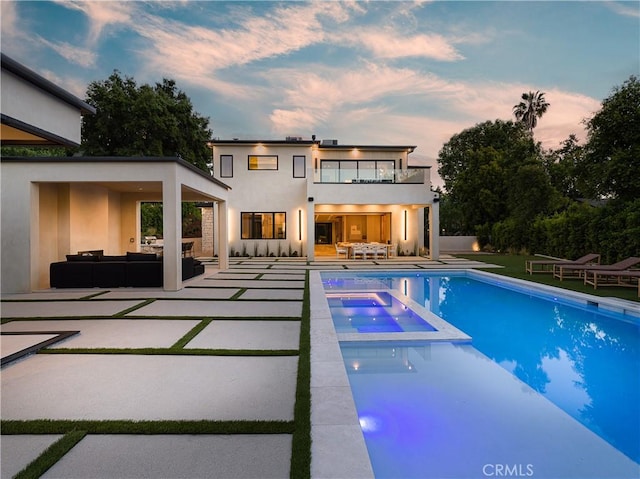 pool at dusk with an in ground hot tub, an outdoor hangout area, and a patio