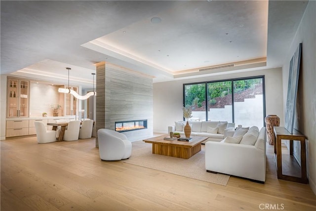 living room with a tile fireplace, light hardwood / wood-style flooring, and a raised ceiling