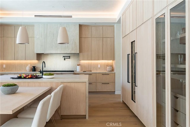 kitchen featuring backsplash, light hardwood / wood-style floors, hanging light fixtures, a breakfast bar area, and light brown cabinetry