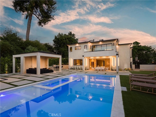 back house at dusk featuring a swimming pool with hot tub, an outdoor living space, and a patio