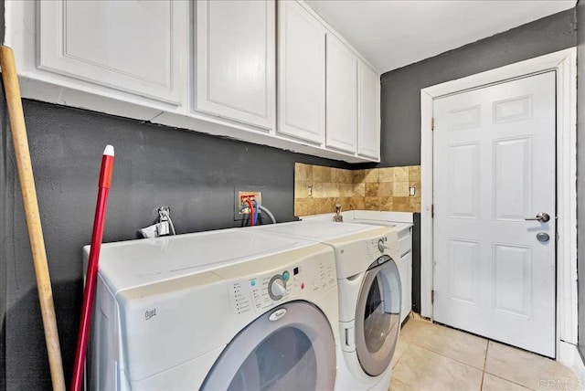 clothes washing area with cabinets, light tile patterned floors, and washing machine and clothes dryer