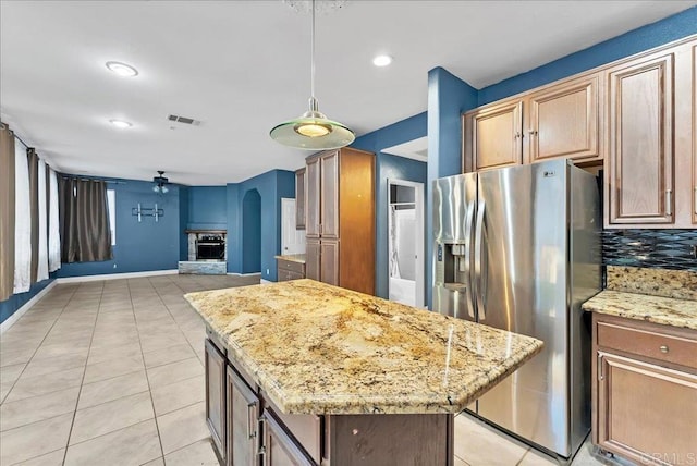 kitchen with a center island, backsplash, a stone fireplace, light stone counters, and stainless steel fridge with ice dispenser