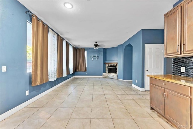 kitchen with ceiling fan, light stone counters, light tile patterned floors, and backsplash