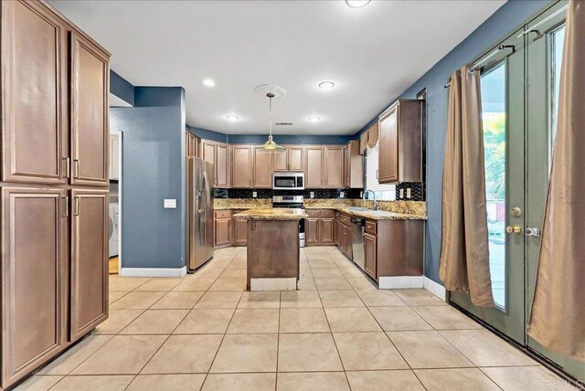 kitchen featuring light stone countertops, a center island, sink, hanging light fixtures, and stainless steel appliances