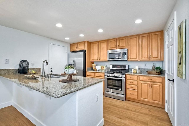 kitchen with appliances with stainless steel finishes, light hardwood / wood-style floors, kitchen peninsula, a breakfast bar, and sink