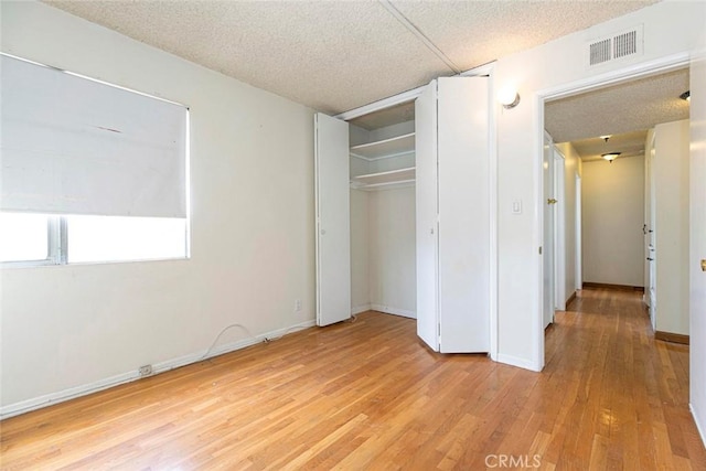 unfurnished bedroom with light wood-type flooring, a closet, and a textured ceiling