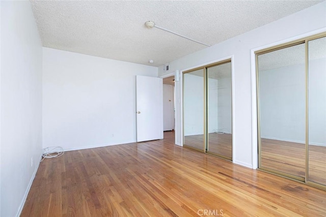 unfurnished bedroom with a textured ceiling, two closets, and wood-type flooring