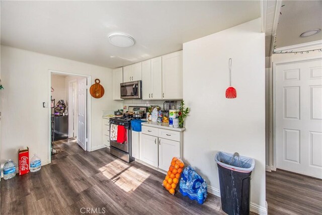 kitchen with dark wood-type flooring, backsplash, white cabinetry, and appliances with stainless steel finishes