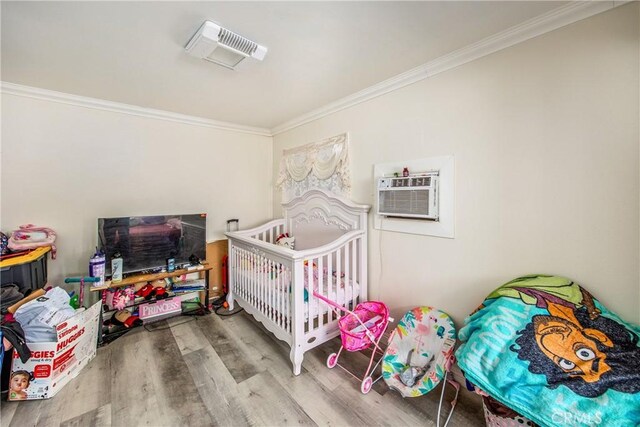 bedroom with a crib, a wall mounted air conditioner, crown molding, and hardwood / wood-style flooring