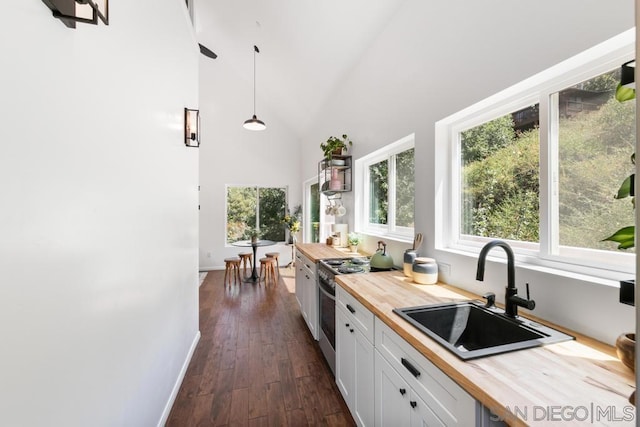 kitchen with decorative light fixtures, stainless steel gas stove, sink, white cabinets, and butcher block counters