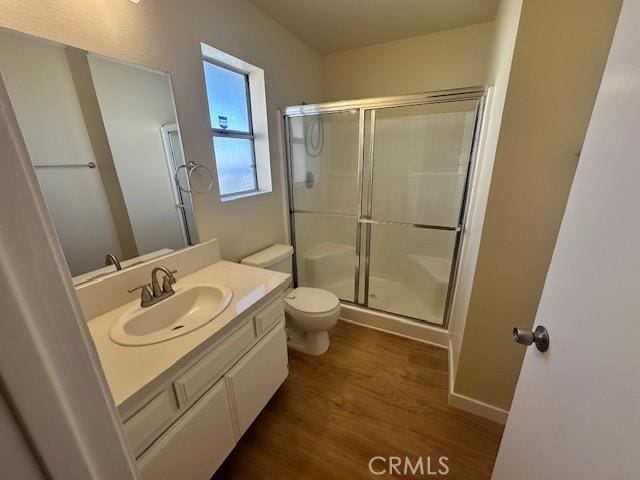 bathroom featuring hardwood / wood-style flooring, toilet, a shower with door, and vanity