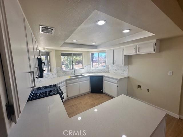 kitchen with range, white cabinets, a raised ceiling, and kitchen peninsula