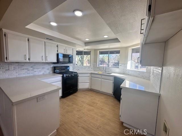 kitchen featuring white cabinetry, a tray ceiling, and black appliances