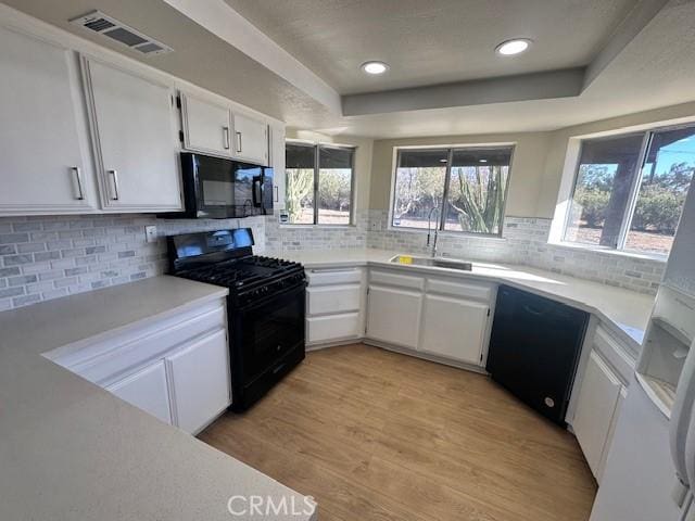 kitchen with white cabinetry, decorative backsplash, a raised ceiling, light hardwood / wood-style flooring, and black appliances