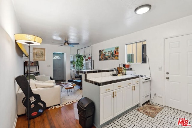 kitchen featuring ceiling fan, tile countertops, kitchen peninsula, white cabinets, and white range oven