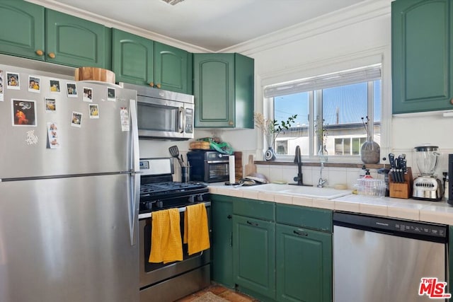 kitchen featuring tile countertops, sink, appliances with stainless steel finishes, green cabinetry, and ornamental molding