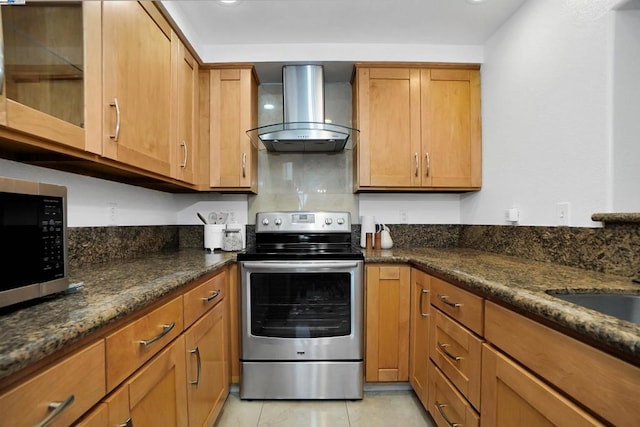 kitchen featuring stainless steel appliances, wall chimney range hood, light tile patterned floors, and dark stone counters