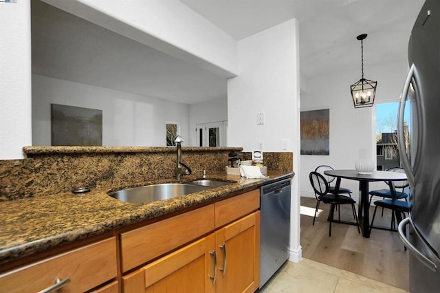 kitchen featuring dark stone countertops, appliances with stainless steel finishes, a notable chandelier, pendant lighting, and sink