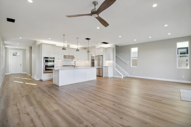 kitchen featuring tasteful backsplash, pendant lighting, a kitchen island with sink, stainless steel appliances, and white cabinets