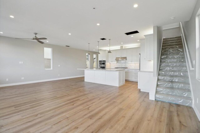 kitchen with decorative light fixtures, white cabinetry, tasteful backsplash, light hardwood / wood-style floors, and an island with sink