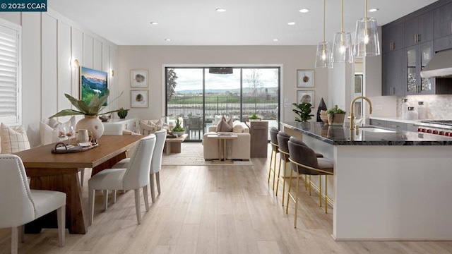 kitchen featuring sink, ventilation hood, dark stone counters, light hardwood / wood-style floors, and decorative light fixtures