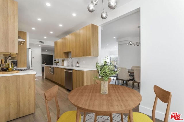 kitchen featuring exhaust hood, light hardwood / wood-style floors, stainless steel dishwasher, pendant lighting, and sink