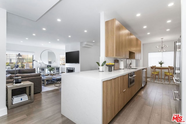 kitchen with light hardwood / wood-style floors, sink, an inviting chandelier, hanging light fixtures, and appliances with stainless steel finishes