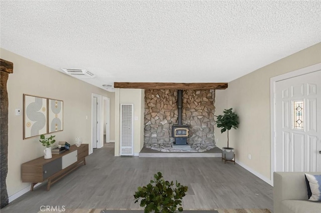 unfurnished living room featuring beam ceiling, a wood stove, hardwood / wood-style floors, and a textured ceiling