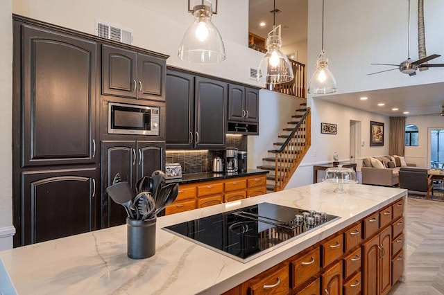 kitchen featuring stainless steel microwave, light parquet flooring, decorative light fixtures, dark stone countertops, and black electric cooktop