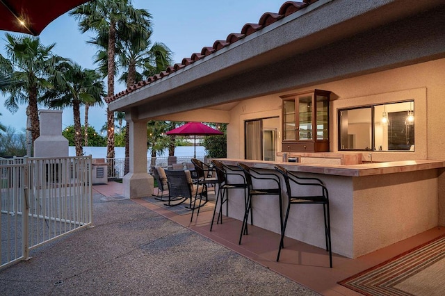 patio terrace at dusk featuring an outdoor fireplace and an outdoor bar