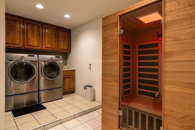 laundry room with washing machine and dryer, light tile patterned flooring, wooden walls, and cabinets