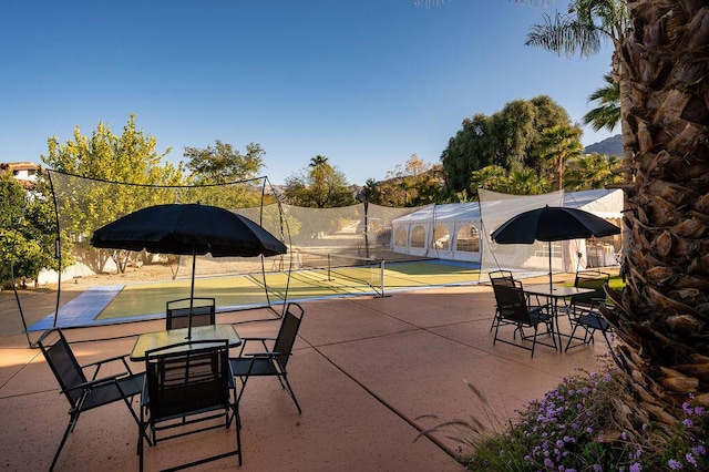 view of patio featuring tennis court and glass enclosure