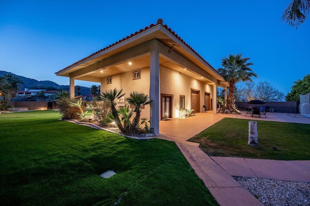 property exterior at dusk with a mountain view, a lawn, and a patio