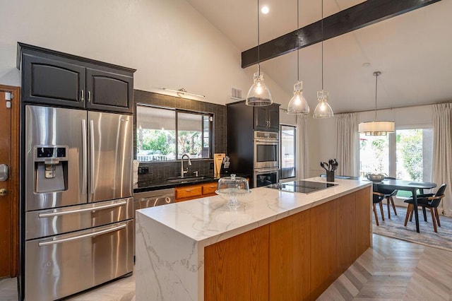 kitchen featuring dark stone countertops, a center island with sink, sink, beamed ceiling, and appliances with stainless steel finishes