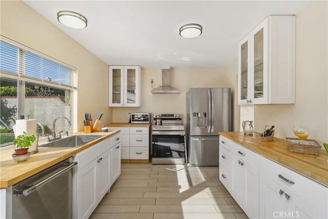 kitchen featuring butcher block countertops, sink, appliances with stainless steel finishes, white cabinetry, and exhaust hood